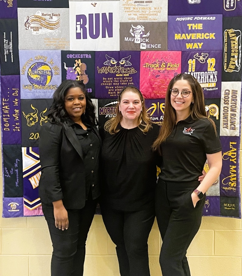 A group of women standing in front of a wall with a signDescription automatically generated